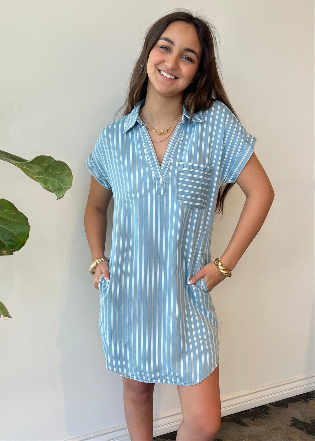 Woman wearing a blue and white striped short-sleeve shirt dress with hands in side pockets 
