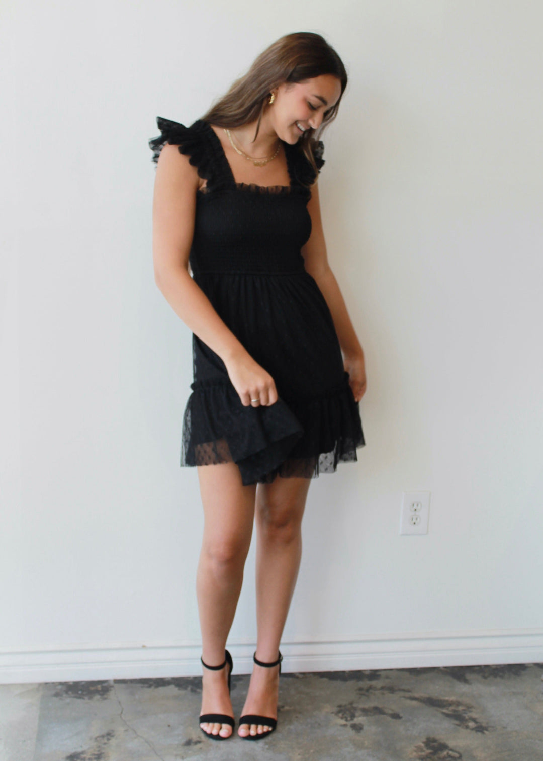 Woman wearing a black dress standing against a white wall.