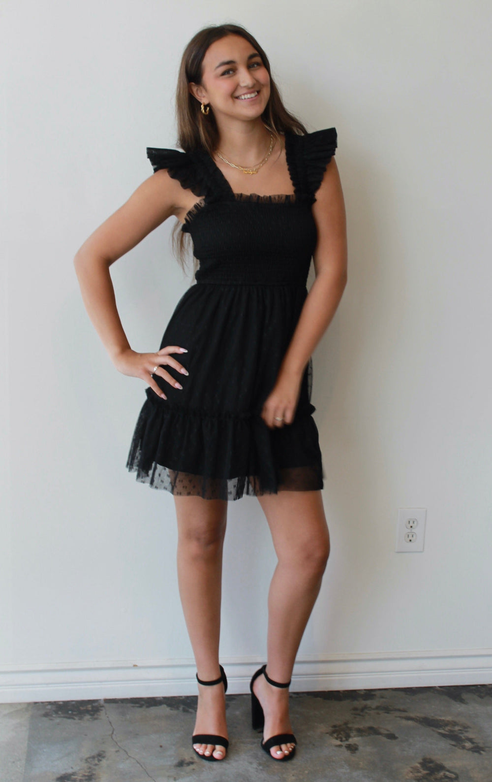 Woman wearing a black dress standing against a white wall.