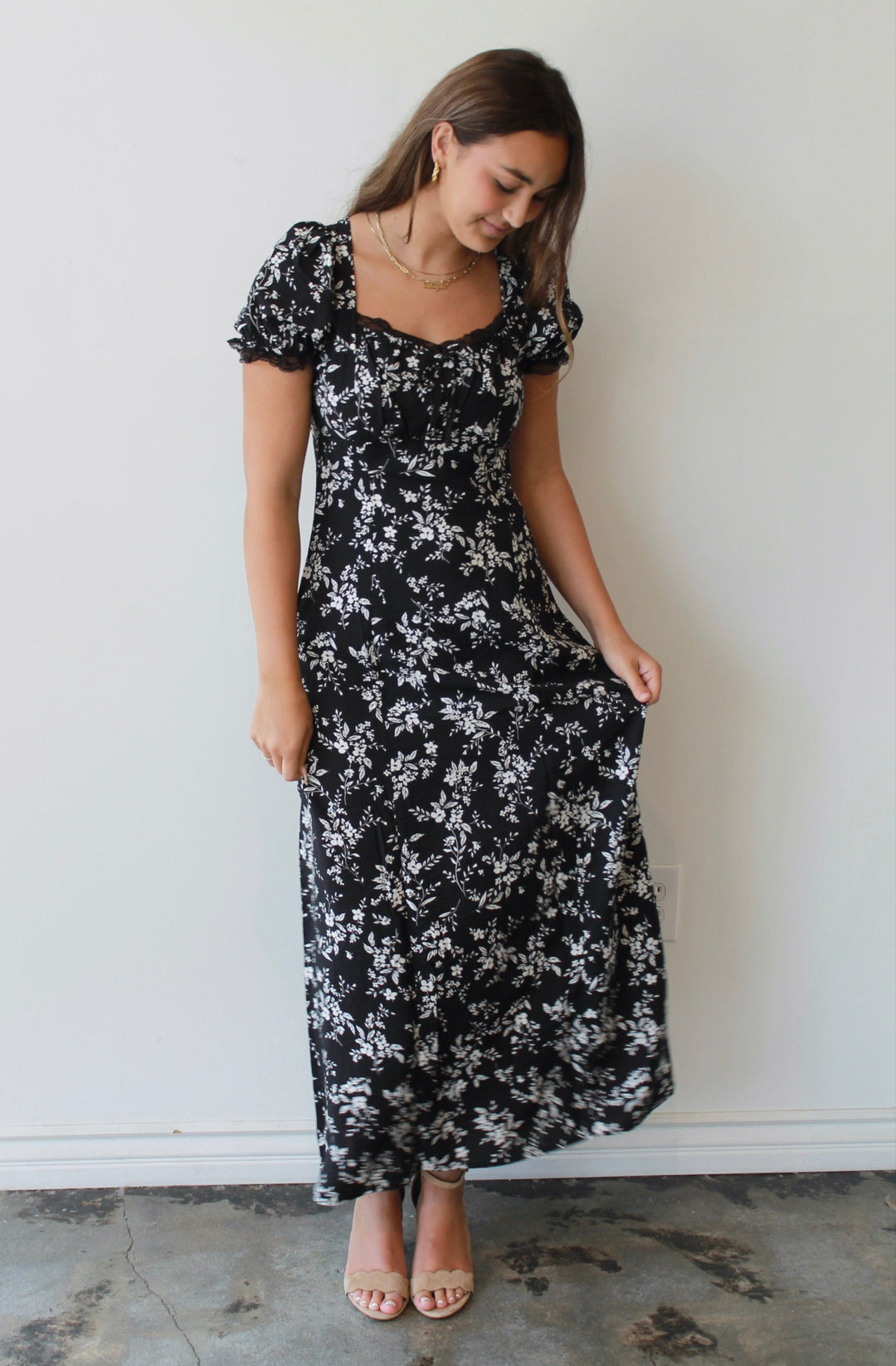 Woman wearing a black floral dress against a white wall.