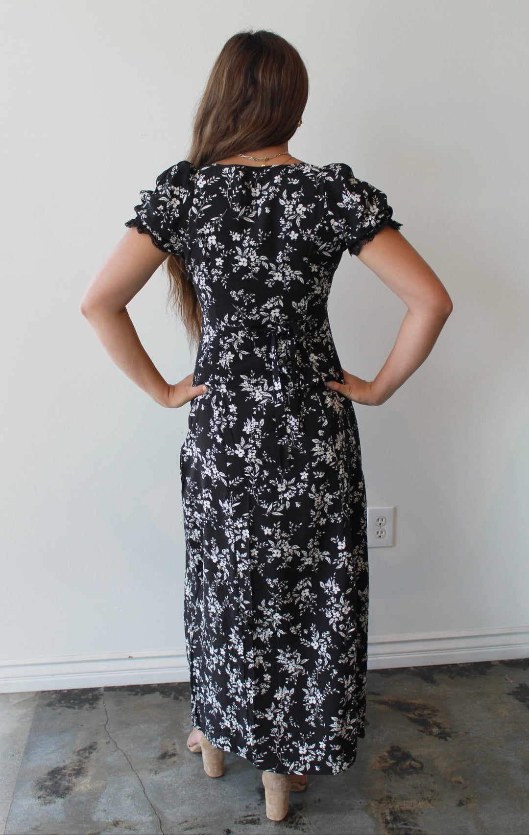 Woman wearing a black floral dress standing against a white wall.