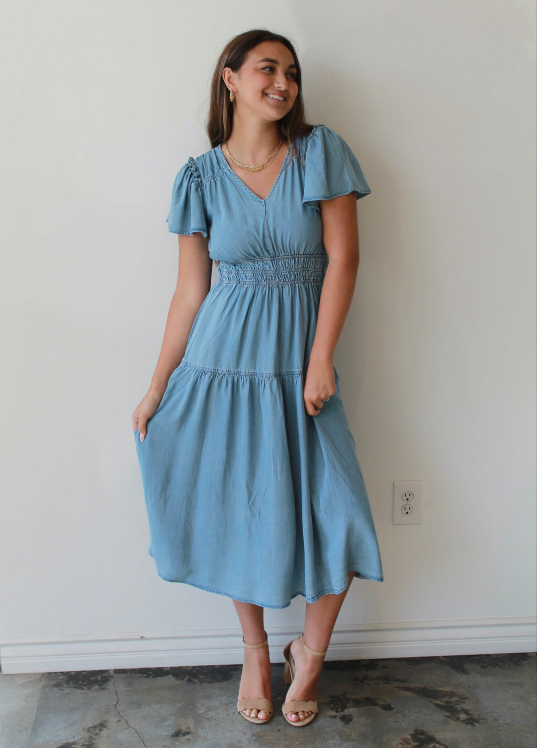 Woman wearing a light blue dress standing against a white wall.
