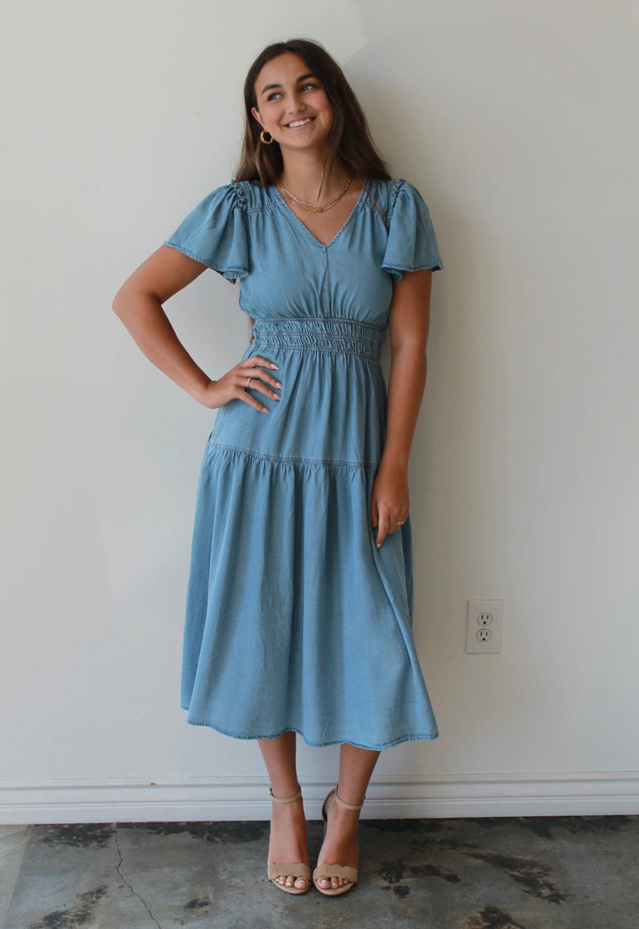 Woman wearing a light blue dress standing against a white wall.