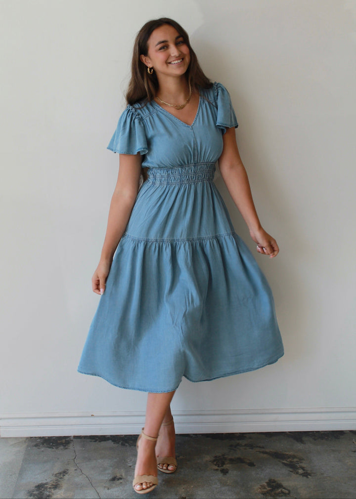 Woman wearing a blue dress standing against a white wall