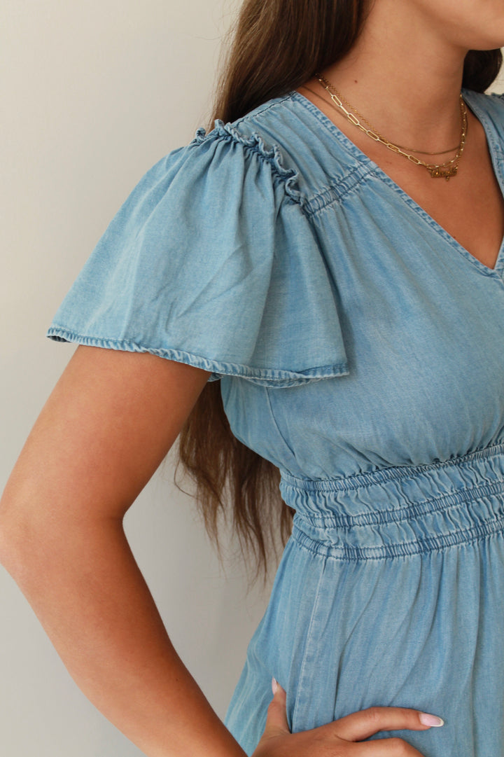 Light blue denim dress with ruffled sleeves worn by a person against a neutral background