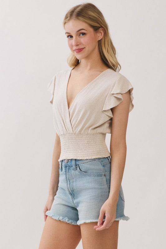 Beige linen wrap top with smocked waist and flutter sleeves shown at angle