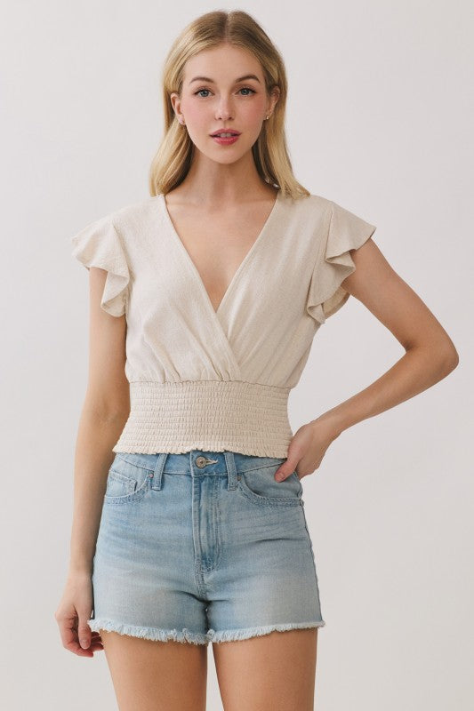 Front view of beige linen wrap top with smocked waist and flutter sleeves